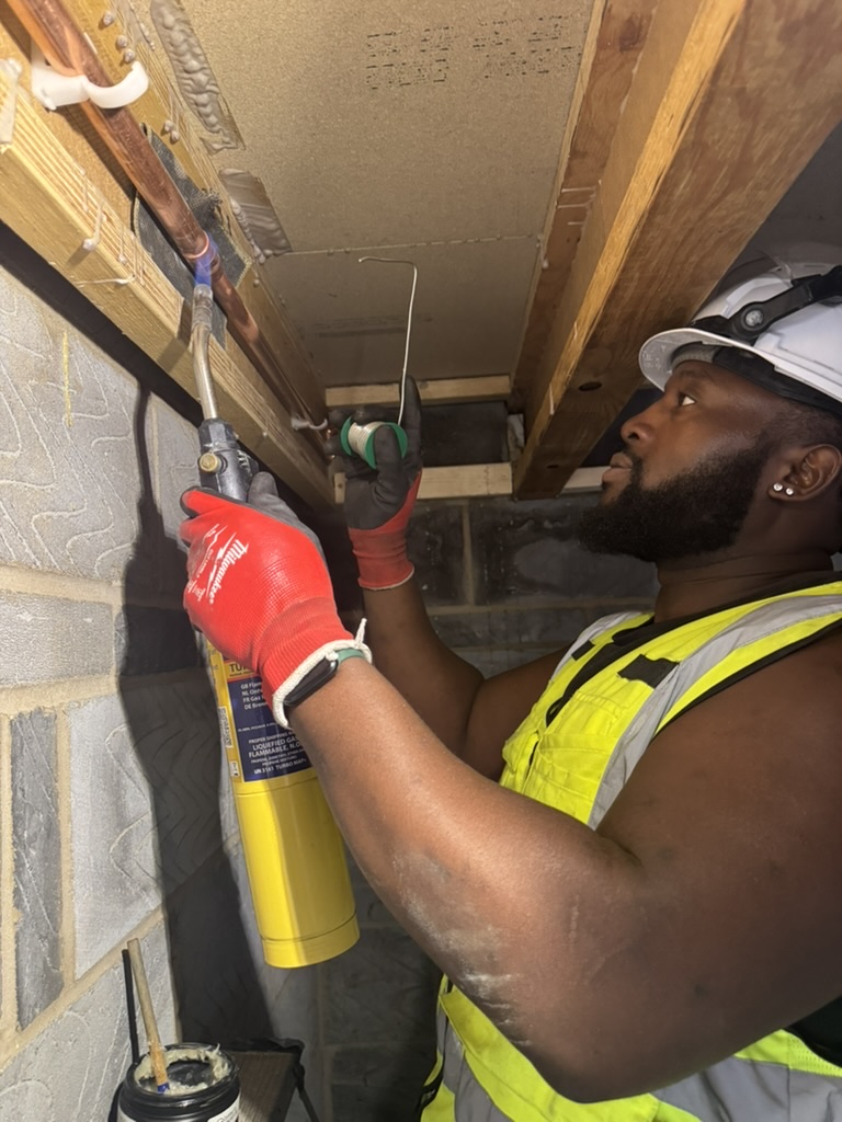 Tee Alausa carefully soldering copper pipework